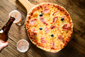 hand pouring fresh beer on a glass with pizza on wood restaurant table indoor with cosy dim light