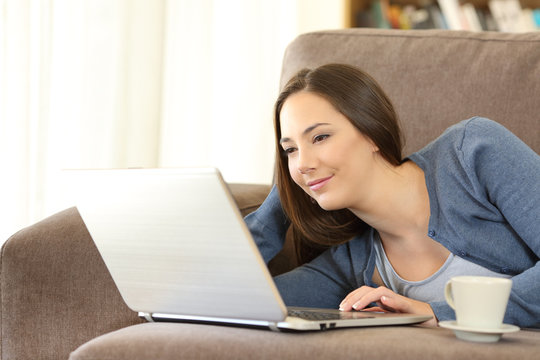 Woman using a laptop lying on a couch at home
