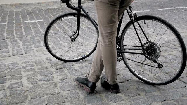 Slow motion footage of stylish young man standing with bicycle on old paved road