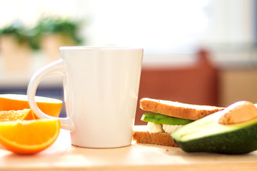 Cup of coffee, oranges and a healthy avocado sandwich for breakfast