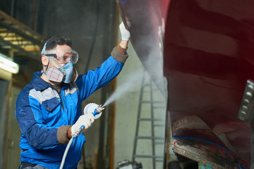 Side view portrait of  worker wearing protective mask spray painting boat in yacht workshop  copy...