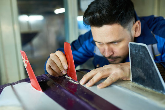 Portrait of mature handsome man  carefully placing fins on custom surfing board  in  workshop, copy space
