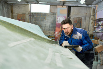 Portrait of handsome worker making notes on clipboard while repairing boat in yacht workshop, copy...