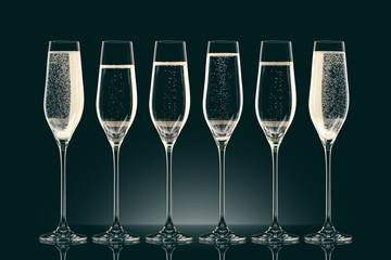 six transparent glasses with different level of champagne on black