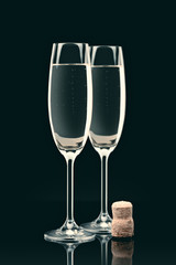 two transparent glasses with calm champagne and cork on table on black