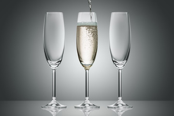 pouring champagne from bottle into three glasses on grey