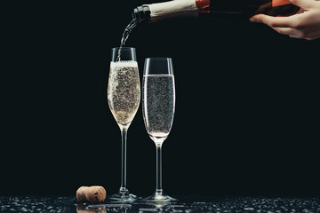 cropped image of woman pouring champagne from bottle into glasses on black - obrazy, fototapety, plakaty