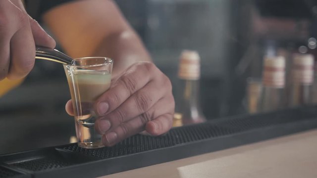 section of unrecognizable bartender pouring alcohol shots at bar counter to little glasses of blue liquid standing in row