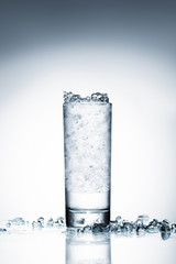 glass of cold water with crushed ice on reflective surface on white