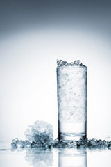 glass of cold water with ice on reflective surface on white