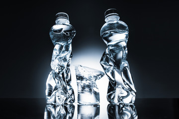 still life with crumpled plastic bottles and water and cup of water on dark