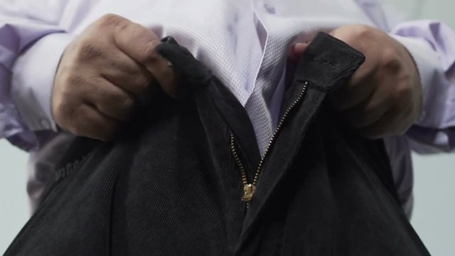 Bottom view of obese male trying to pull his pants zipper, mans health, closeup