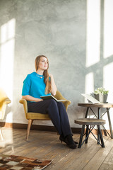 Fototapeta premium Cheerful Woman with Book and Laptop at Home Office. Woman Working with New Startup Project in Modern Loft