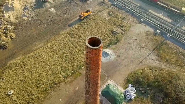 Aerial: Drone flying round old abandoned red clay brick build factory chimney. Few pigeons relaxing at the top of the chimney.