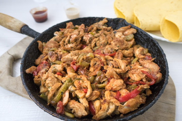 Chicken stew with red and green pepper, with red onion, pickled cucumber and spices in a frying pan.