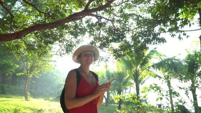 Woman close up. girl using a phone texting on smartphone app on grasses in garden. Vietnam. The smiling woman travels with a backpack around the island