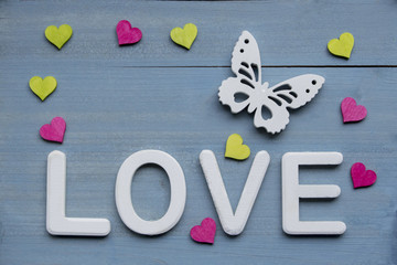 LOVE weisse Schrift weisser Schmetterling und pink und grüne Herzen auf blau gebeiztem Hintergrund aus Holz