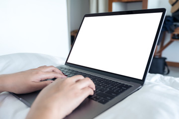 Mockup image of woman's hands using and typing on laptop with blank white desktop screen keyboard on the bed