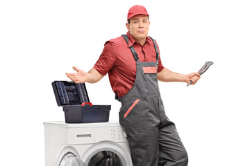 Uncertain repairman with a wrench leaning against a washing machine