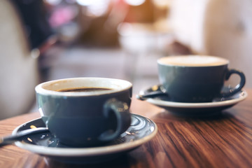Closeup image of two blue cups of hot latte coffee and Americano coffee on vintage wooden table in cafe