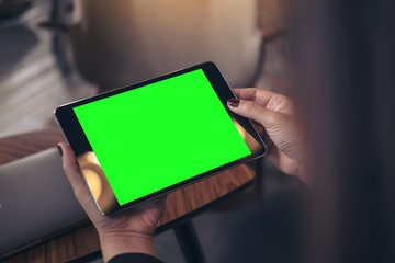 Mockup image of woman's hands holding and looking at black tablet pc with blank green desktop screen in cafe