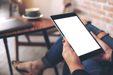 Mockup top view image of a woman wearing ripped jean sitting cross legged , holding black tablet pc with blank white desktop screen on thigh in cafe
