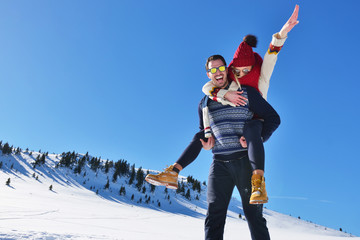 Young couple having fun on snow. Happy man at the mountain giving piggyback ride to his smiling...
