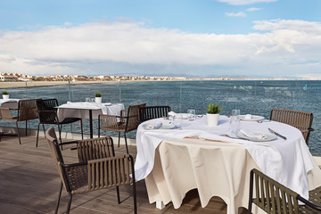 Empty dining tables on terrace with  beautiful view of ocean, on  sunny day.