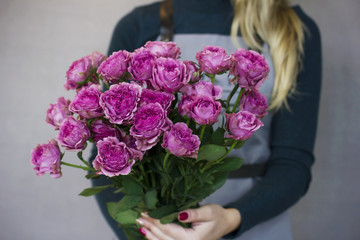 The big bouquet of pink roses in female hands on gray background