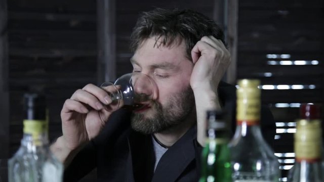 drunk man drinks alcohol, lot of empty bottles around him
