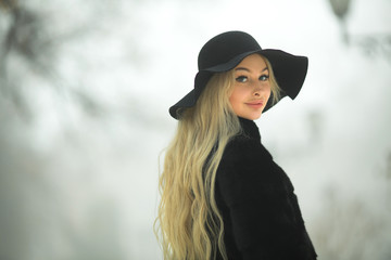 beautiful young girl in fur coat and hat walking in the park in winter weather