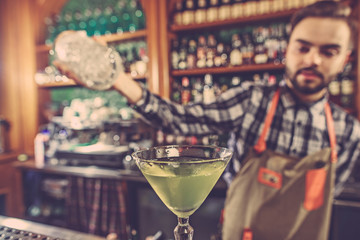 Barman making an alcoholic cocktail at the bar counter on the bar background