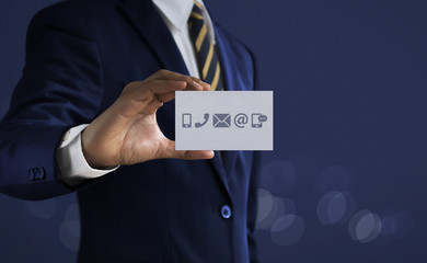 Customer service, call center service or contact us concept Businessman holding communication icons (mobile phone, telephone, mail, email, social media) card on dark tone background.