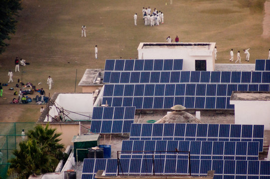 Children in white cricket uniforms playing on a field powered by solar panels. Perfect example of how alternate sources of energy are being adopted for public buildings in Noida Delhi