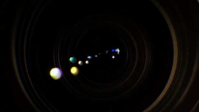 A close-up of the lens of a video camera. The light source illuminates the lenses, then goes into darkness