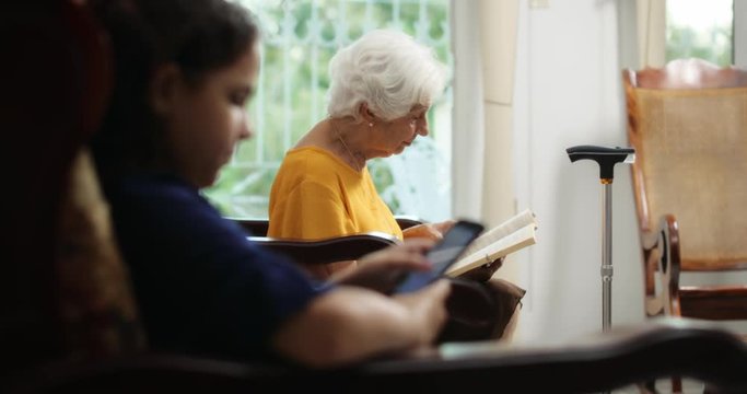Granddaughter Using Mobile Phone And Grandma Reading Book