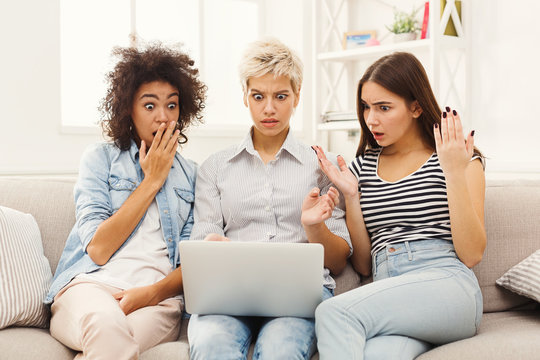 Three beautiful shocked women using laptop at home