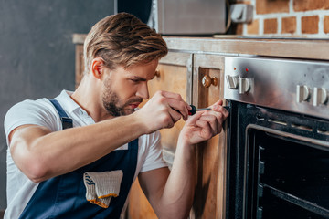 handsome young repairman fixing oven with screwdriver