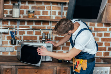 professional young foreman repairing microwave oven in kitchen
