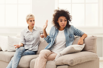 Two female friends sitting on sofa and arguing
