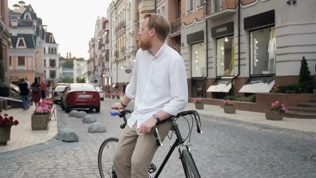 Slow motion video of handsome bearded man sitting on bicycle on street