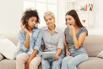 Three surprised female friends using tablet.