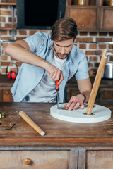 handsome young man repairing stool with screwdriver