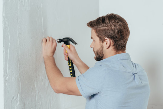 Young Man Hammering Nail In Wall At Home