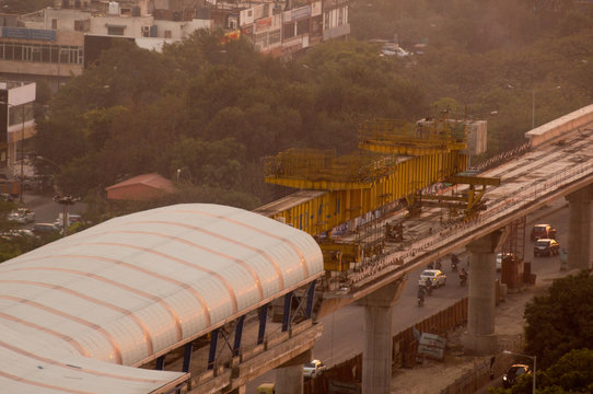 Aerial photograph of a metro track laying machine working on an under construction track in Delhi, Lucknow, bangalore. Shot on a foggy golden hour evening. The metro is a critical public transport