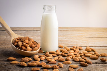 almond milk in bottle with Almonds pour from wood spoon