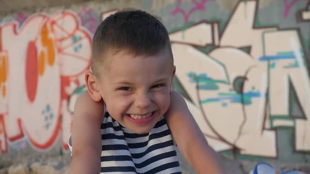 portrait of a playful little boy in a striped shirt who yells, grimaces and smiling looking at camera on the background wall with graffiti