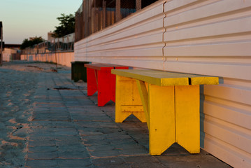 multi-colored green yellow red bench on a background of stone gray tiles and sand, beach, white fence