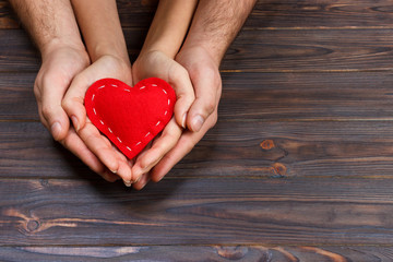 Love, family concept. Close up of man and woman hands holding red rubber heart together