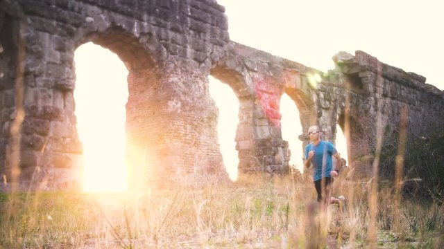 Young man in sportswear running along ancient roman aqueduct Appio Claudio. Training outdoor alone in peaceful park in Rome at sunset slow motion.